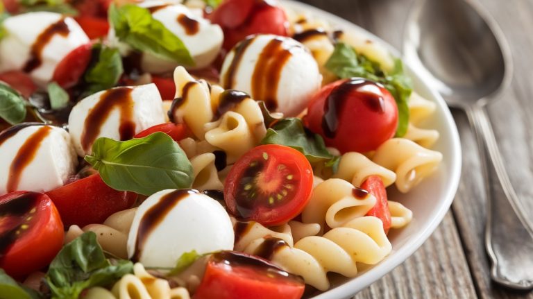 Caprese Pasta Salad with rotini pasta, cherry tomatoes, mozzarella balls, fresh basil, and a balsamic olive oil dressing in a white serving bowl.